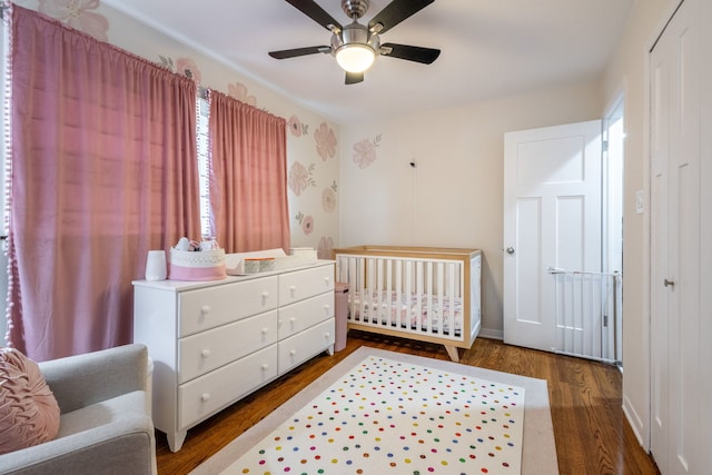 bedroom with a nursery area, a closet, wood finished floors, and ceiling fan
