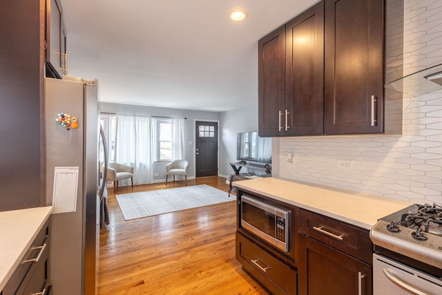 kitchen featuring stainless steel appliances, open floor plan, light wood-type flooring, backsplash, and light countertops