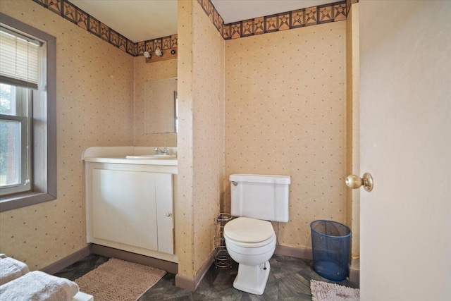 bathroom featuring toilet, wallpapered walls, vanity, and baseboards