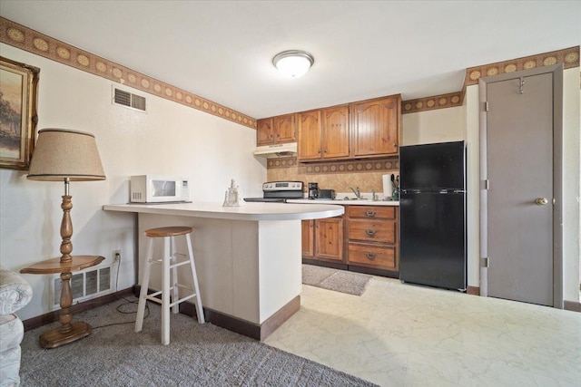 kitchen with white microwave, visible vents, freestanding refrigerator, electric stove, and brown cabinetry