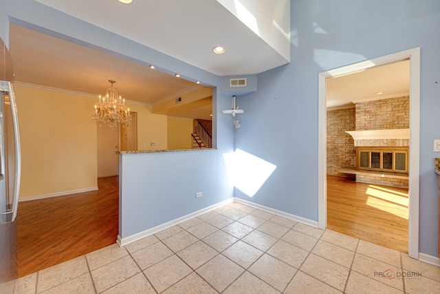 spare room featuring light hardwood / wood-style flooring, brick wall, a brick fireplace, and crown molding