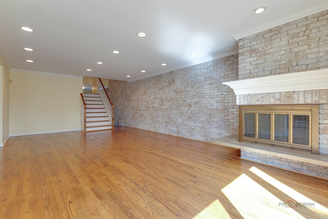 unfurnished living room with crown molding, brick wall, light hardwood / wood-style flooring, and a brick fireplace