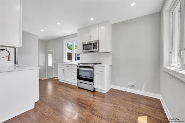 kitchen with tasteful backsplash, dark hardwood / wood-style flooring, white cabinets, and stainless steel appliances