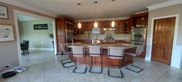 kitchen with light stone countertops, a kitchen island with sink, built in appliances, backsplash, and light tile floors