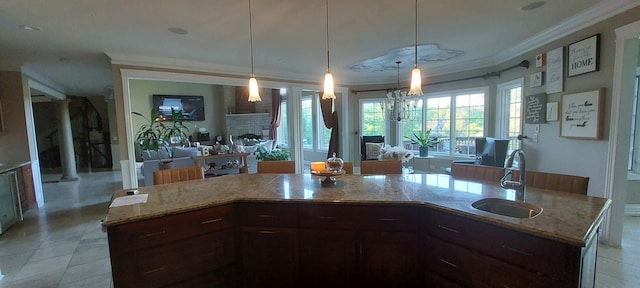 kitchen with light stone counters, a kitchen island with sink, sink, light tile floors, and pendant lighting