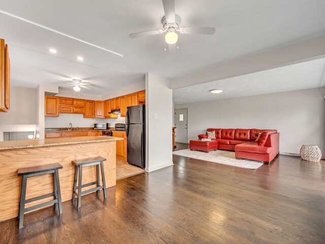 kitchen featuring kitchen peninsula, appliances with stainless steel finishes, a kitchen bar, sink, and light hardwood / wood-style flooring