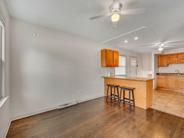 kitchen with kitchen peninsula, light stone counters, a breakfast bar, ceiling fan, and wood-type flooring