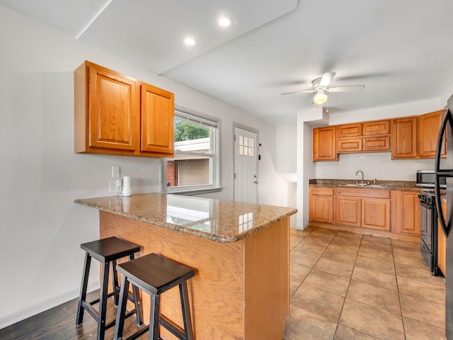 kitchen with a kitchen breakfast bar, sink, ceiling fan, light stone countertops, and kitchen peninsula