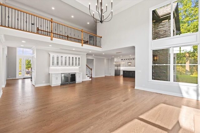 unfurnished living room featuring a chandelier, a high ceiling, hardwood / wood-style flooring, and ornamental molding