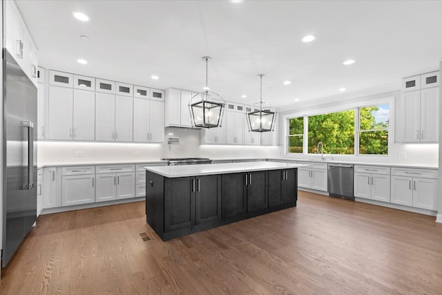 kitchen with appliances with stainless steel finishes, a kitchen island, light hardwood / wood-style flooring, white cabinetry, and hanging light fixtures