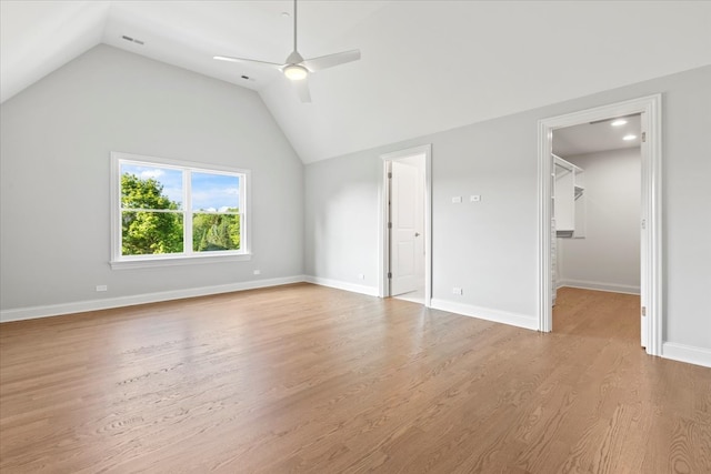 unfurnished bedroom featuring lofted ceiling, a walk in closet, light hardwood / wood-style flooring, ceiling fan, and a closet