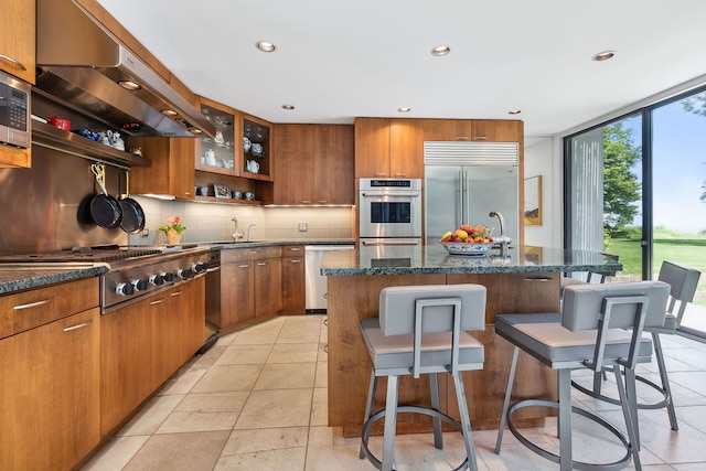 kitchen featuring extractor fan, built in appliances, backsplash, light tile floors, and a kitchen island with sink