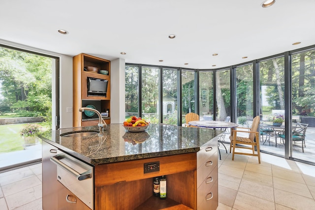 kitchen featuring sink, dark stone counters, a kitchen island with sink, light tile patterned floors, and floor to ceiling windows