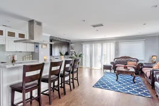 kitchen with tasteful backsplash, a breakfast bar, island exhaust hood, hardwood / wood-style flooring, and white cabinets