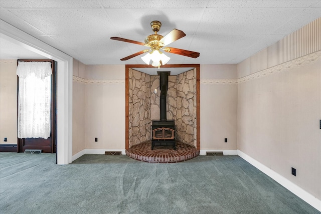 unfurnished living room featuring dark colored carpet, a wood stove, and ceiling fan