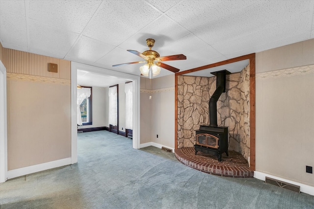 unfurnished living room with a wood stove, carpet flooring, and ceiling fan