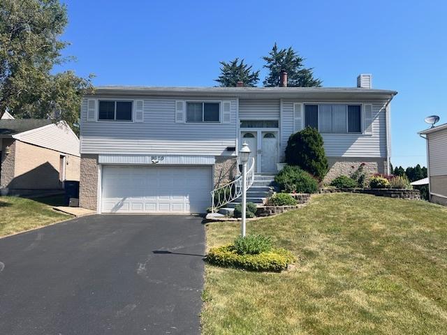 split foyer home featuring a garage, entry steps, driveway, a front lawn, and brick siding