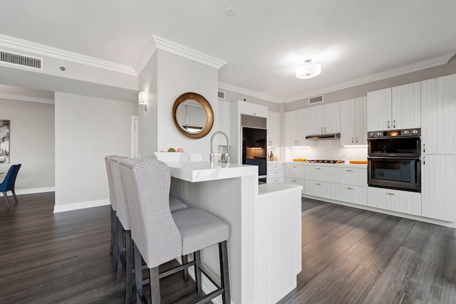 kitchen featuring a center island with sink, white cabinets, crown molding, dark hardwood / wood-style floors, and double oven