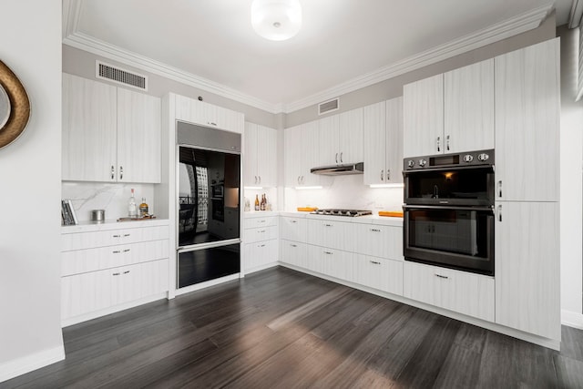 kitchen featuring dark wood-type flooring, backsplash, built in refrigerator, black double oven, and stainless steel gas stovetop