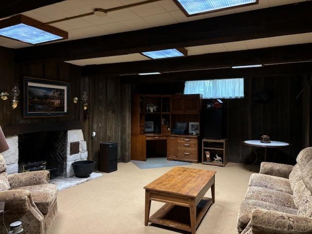 carpeted living room with beamed ceiling, a fireplace, and wood walls