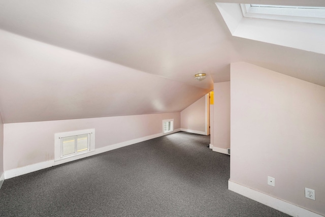 bonus room with dark carpet and vaulted ceiling with skylight