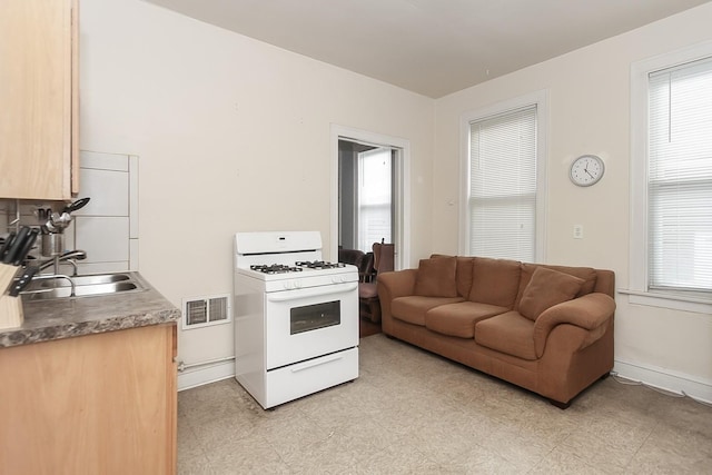 kitchen featuring light brown cabinetry, white gas range oven, and sink