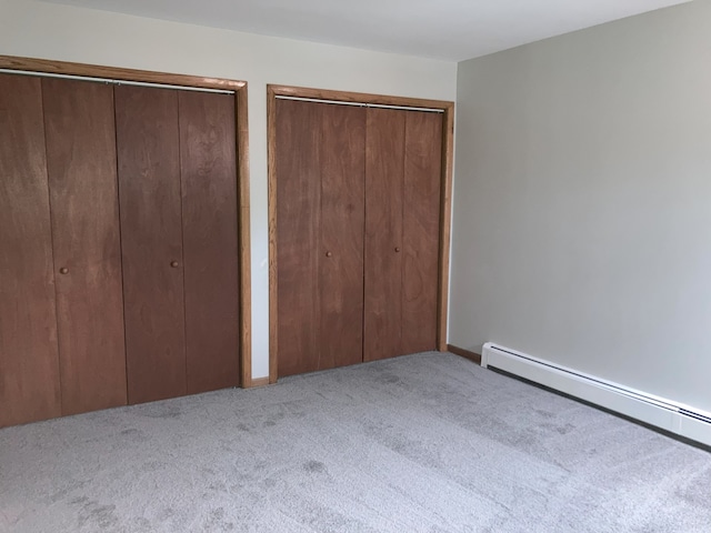 unfurnished bedroom with a baseboard heating unit, two closets, and light colored carpet