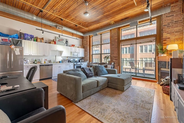 living room with sink, brick wall, a high ceiling, and light wood-type flooring