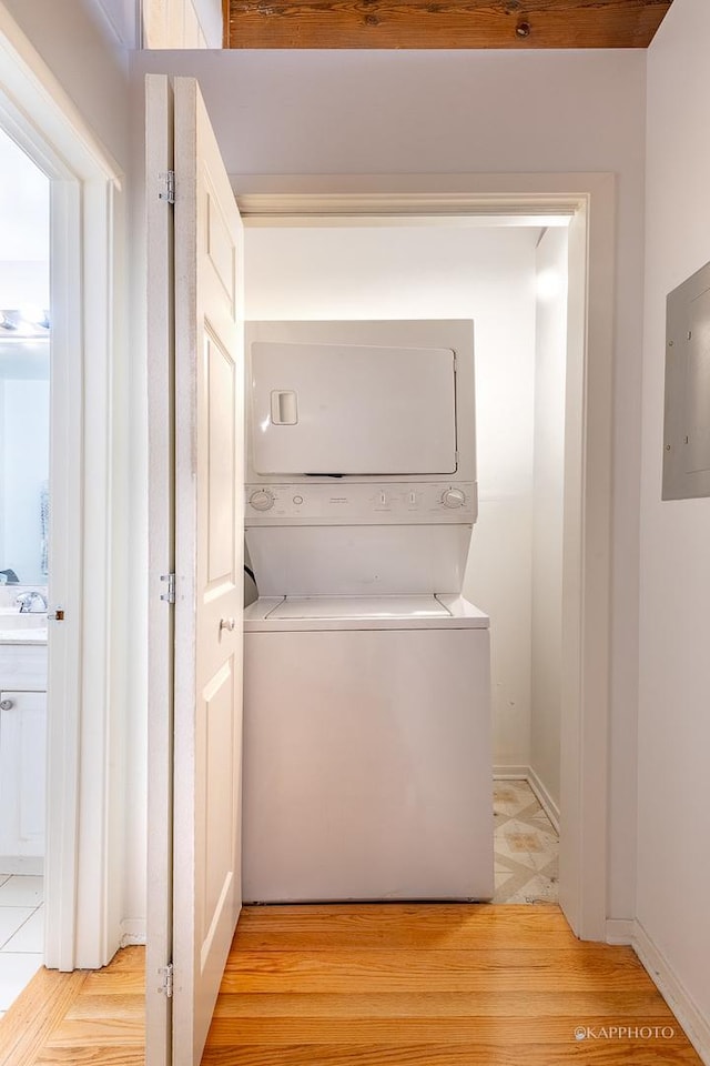 laundry area with light wood-type flooring, electric panel, and stacked washer / dryer