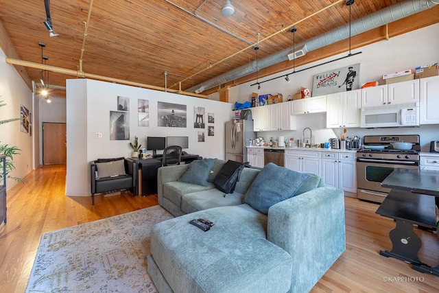 living room with light hardwood / wood-style floors, a towering ceiling, sink, and wood ceiling