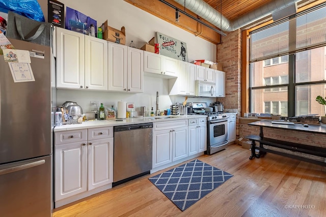 kitchen featuring light wood-type flooring, brick wall, stainless steel appliances, sink, and white cabinetry