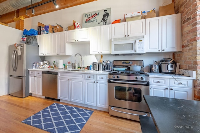 kitchen featuring sink, white cabinets, brick wall, and appliances with stainless steel finishes