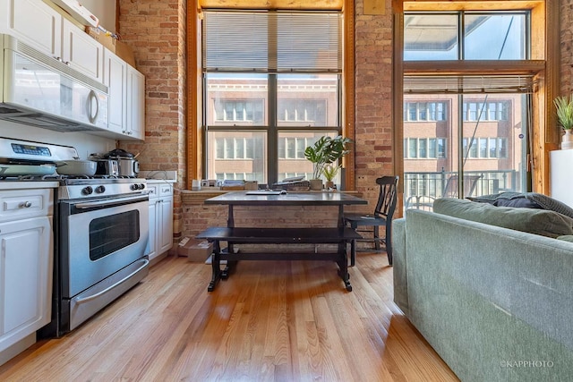 kitchen featuring stainless steel gas range oven, light wood-type flooring, white cabinetry, and brick wall