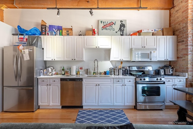 kitchen featuring brick wall, white cabinetry, sink, and appliances with stainless steel finishes