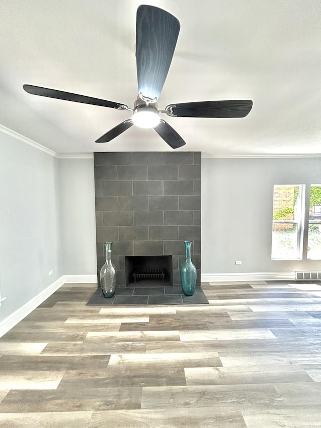 interior details featuring wood-type flooring, ornamental molding, and a tiled fireplace