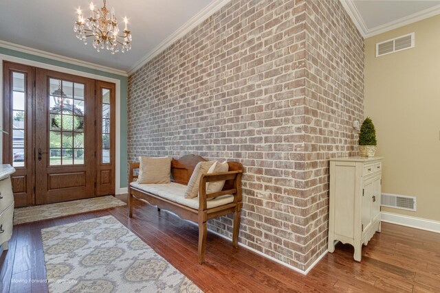 foyer entrance with brick wall, ornamental molding, hardwood / wood-style floors, and an inviting chandelier