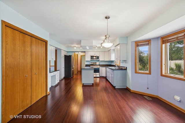 kitchen with stainless steel appliances, dark wood-style flooring, a sink, baseboards, and dark countertops