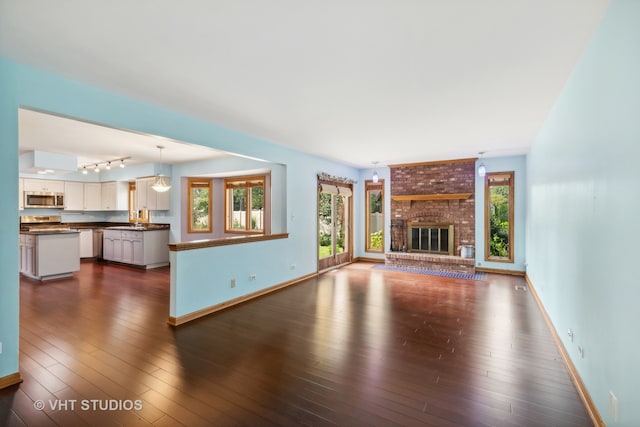 unfurnished living room with a fireplace, dark hardwood / wood-style floors, and a healthy amount of sunlight