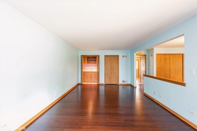 unfurnished room with visible vents, baseboards, and dark wood-type flooring