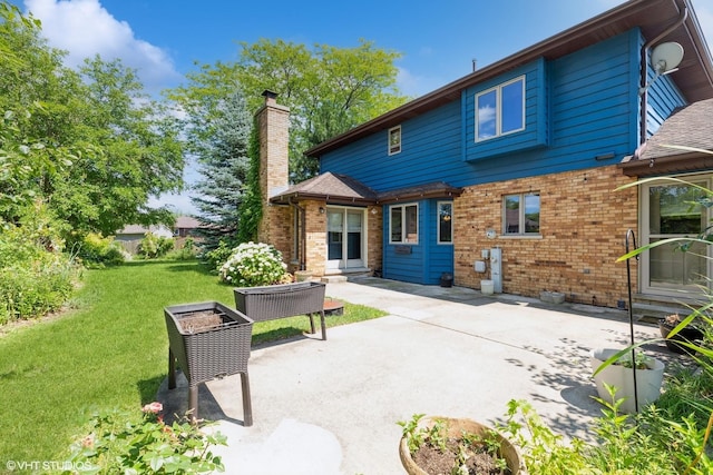 back of property with a yard, brick siding, a chimney, and a patio area