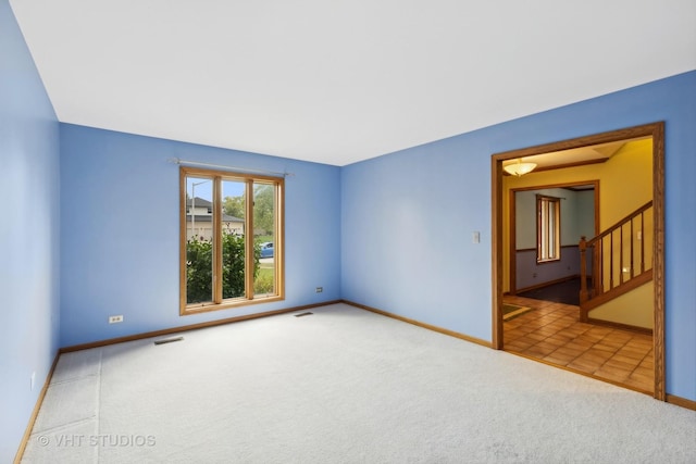 carpeted empty room with visible vents, stairway, and baseboards