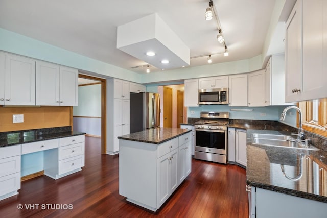 kitchen with built in study area, appliances with stainless steel finishes, dark stone countertops, dark wood-type flooring, and a sink