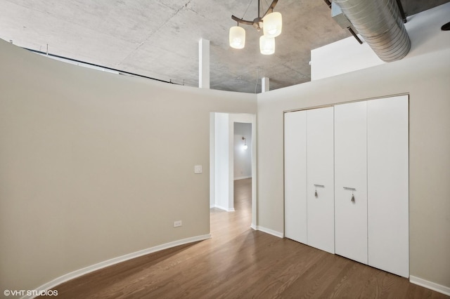 unfurnished bedroom featuring an inviting chandelier, wood-type flooring, and a closet