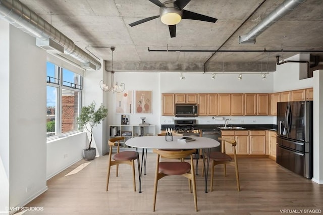 kitchen with appliances with stainless steel finishes, a towering ceiling, sink, hanging light fixtures, and light hardwood / wood-style floors