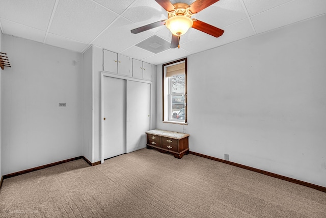 unfurnished bedroom featuring a closet, a paneled ceiling, carpet flooring, and ceiling fan