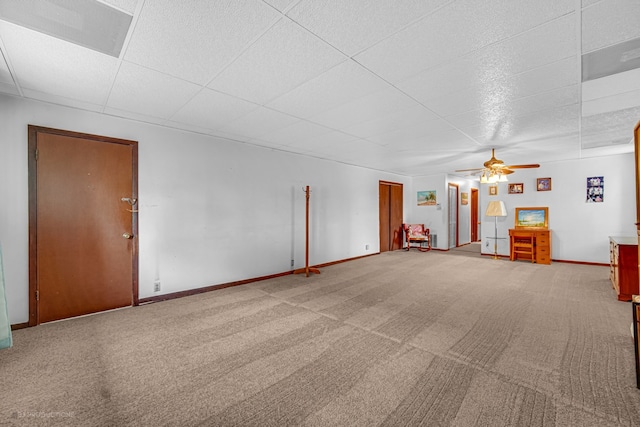 unfurnished living room with ceiling fan, carpet floors, and a drop ceiling