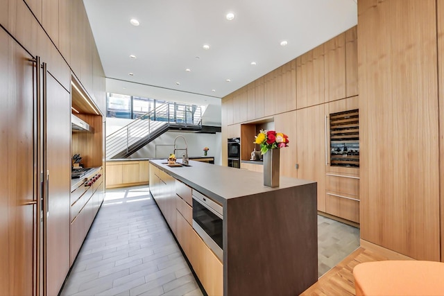 kitchen with light brown cabinets, light hardwood / wood-style floors, built in appliances, an island with sink, and sink