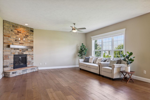 living area with ceiling fan, baseboards, hardwood / wood-style floors, a fireplace, and a textured ceiling