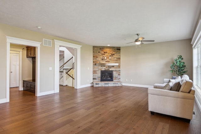 living room with dark wood-style floors, visible vents, baseboards, ceiling fan, and a stone fireplace