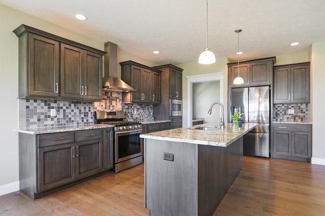 kitchen with light wood-style flooring, a sink, stainless steel appliances, wall chimney exhaust hood, and light stone countertops